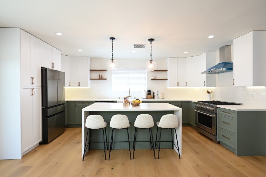Two-tone kitchen with sage green lower cabinets, white uppers, and quartz island with boucle bar stools by RnD Builders Inc