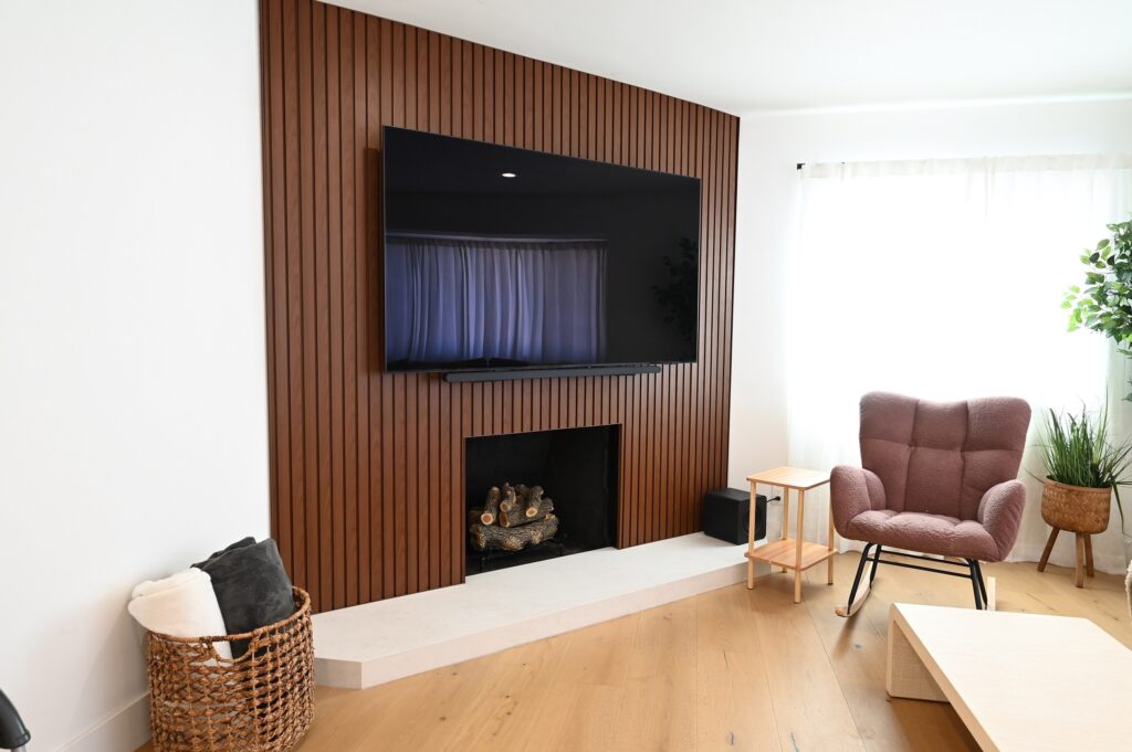 Modern Living Room with Walnut Slat Accent Wall West Hills full remodel: Modern living room with walnut slat accent wall, fireplace, and wall-mounted TV in West Hills by RnD Builders Inc