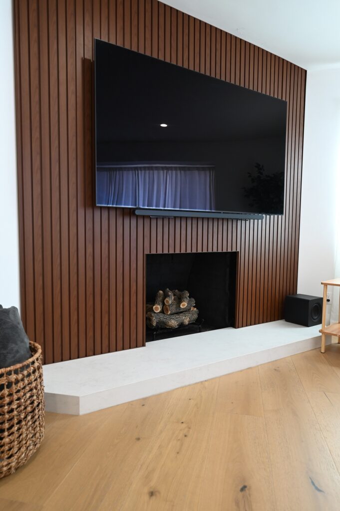 Modern Living Room Feature Wall Modern living room feature wall with vertical walnut slat paneling, built-in fireplace, and wall-mounted TV by RnD Builders Inc