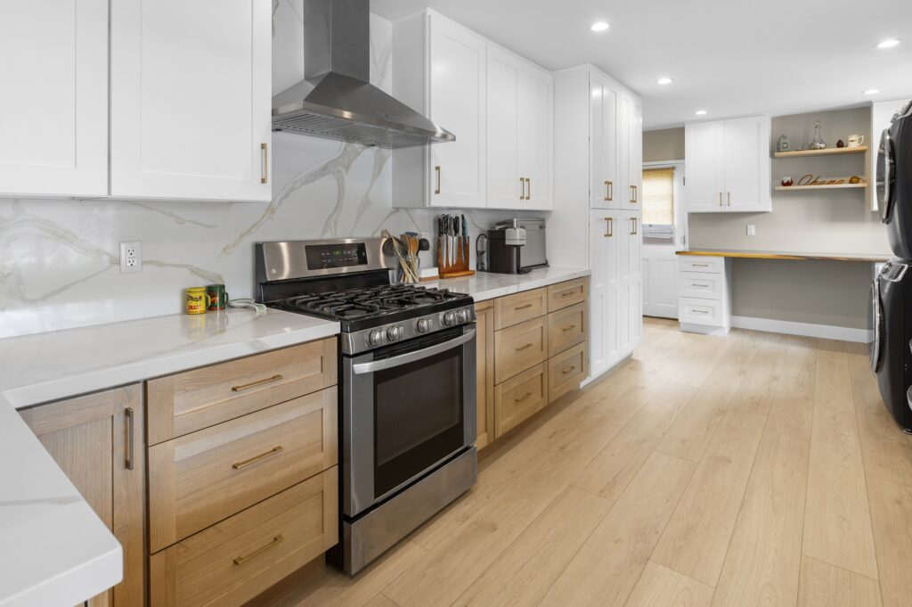 Two-tone kitchen with white upper cabinets, natural oak lower cabinets, quartz countertops, and stainless steel gas range by RnD Builders Inc