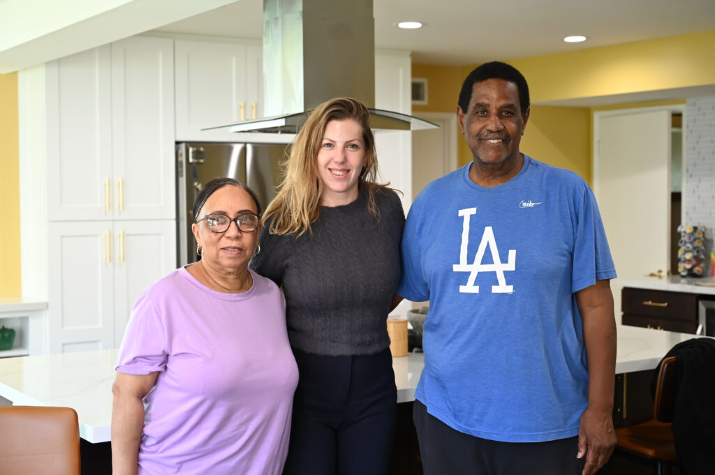 Three people smiling in a remodeled kitchen with white shaker cabinets and stainless steel range hood by RnD Builders Inc