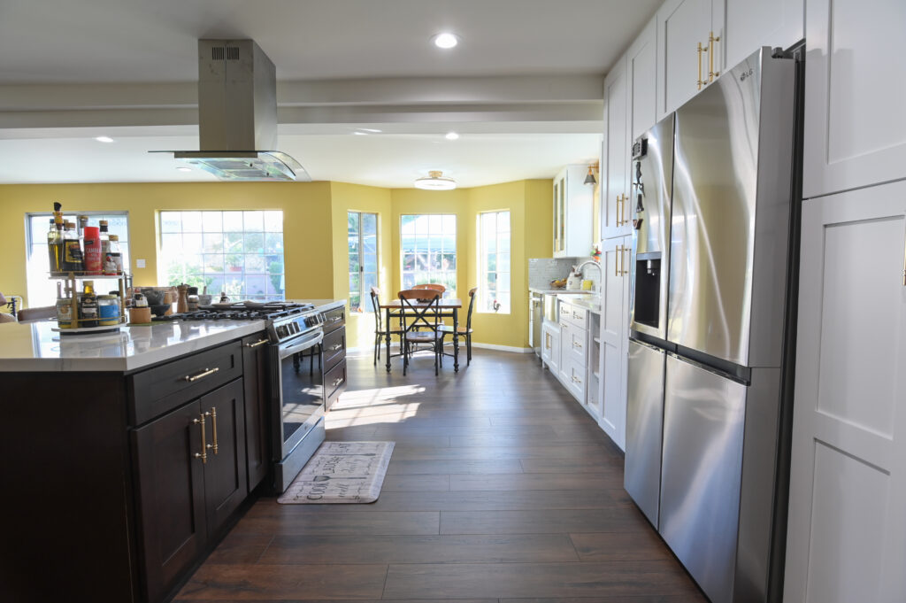Open-concept kitchen with dark island, white shaker cabinets, stainless steel appliances, and yellow accent walls by RnD Builders Inc
