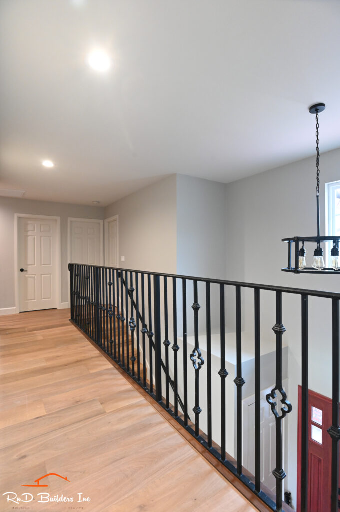 Second-floor hallway with black wrought iron baluster railing and light oak hardwood flooring in Newbury Park by RnD Builders Inc