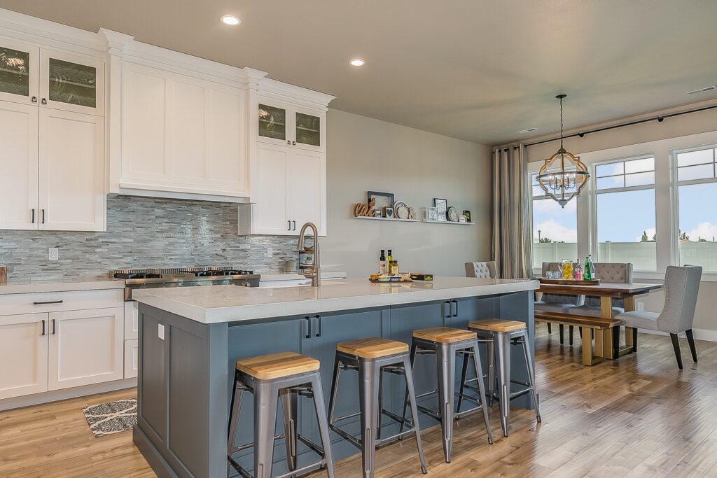Open-concept kitchen with white shaker cabinets, slate-blue island, and metal bar stools in Oxnard by RnD Builders Inc