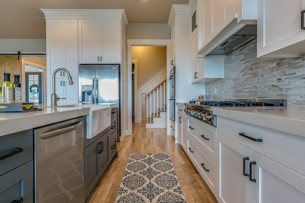 Oxnard kitchen remodel: White shaker cabinet kitchen with farmhouse sink, stainless appliances, and stone mosaic backsplash in Oxnard by RnD Builders Inc