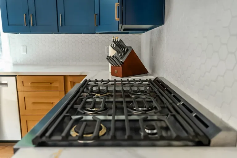 Thousand Oaks home transformation: Kitchen with navy upper cabinets, gas cooktop, white quartz countertop, and hexagon tile backsplash in Thousand Oaks by RnD Builders Inc
