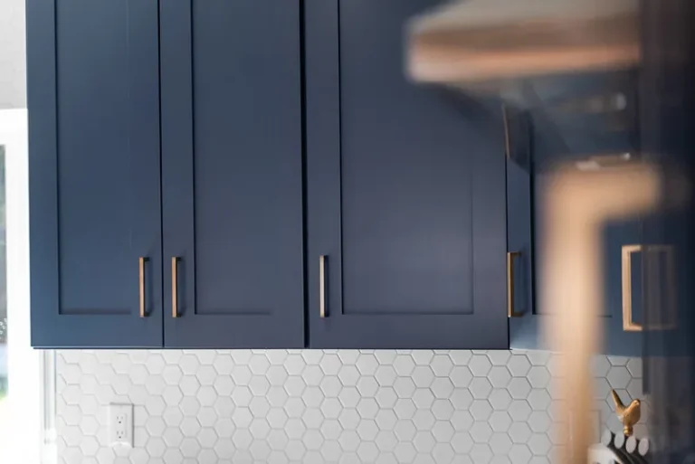 Navy blue shaker upper cabinets with brass pulls above white hexagon tile backsplash in Thousand Oaks by RnD Builders Inc