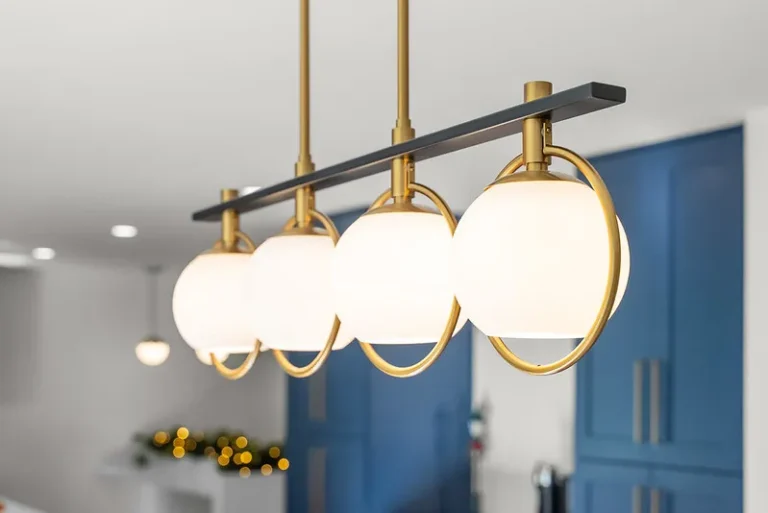 Four-globe brass and matte black linear pendant light fixture over kitchen with blue cabinetry in Thousand Oaks by RnD Builders Inc