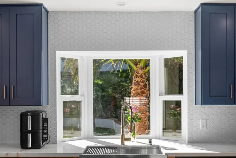 Navy blue shaker cabinets with white hexagon tile backsplash and garden window above stainless sink in Thousand Oaks by RnD Builders Inc