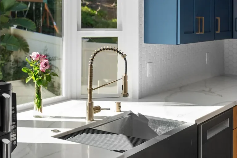 Modern kitchen sink area with brass faucet, white quartz countertop, and navy blue cabinets in Thousand Oaks by RnD Builders Inc