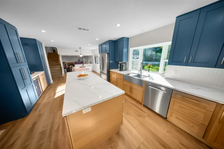Thousand Oaks home transformation: Open-concept kitchen with navy blue upper cabinets, natural wood lower cabinets, white quartz island, and stainless steel appliances in Thousand Oaks by RnD Builders Inc