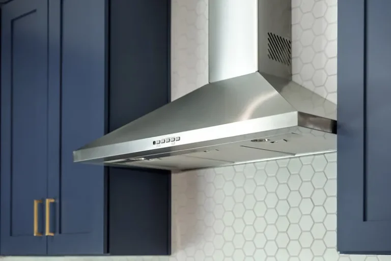 Thousand Oaks home transformation: Stainless steel wall-mount range hood with navy blue cabinets and white hexagon tile backsplash in Thousand Oaks by RnD Builders Inc