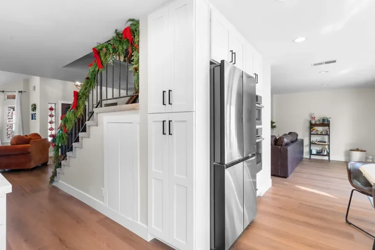 White shaker pantry cabinets with stainless steel refrigerator beside holiday-decorated staircase in Moorpark by RnD Builders Inc