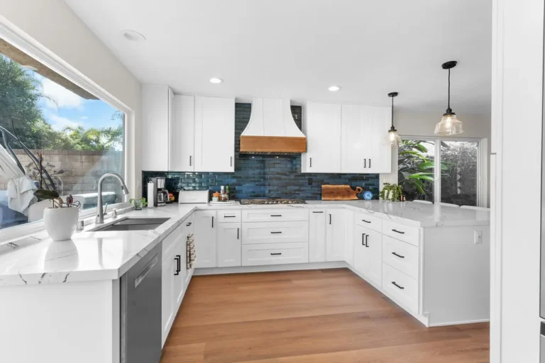 Bright white shaker kitchen with navy subway tile backsplash and wood-accented range hood in Moorpark by RnD Builders Inc