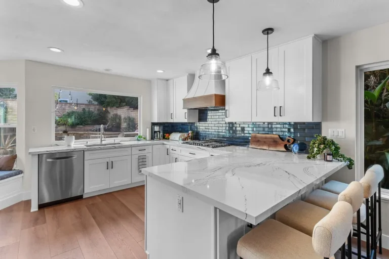 White shaker kitchen with quartz waterfall island, blue subway tile backsplash, and wood accent range hood in Moorpark by RnD Builders Inc
