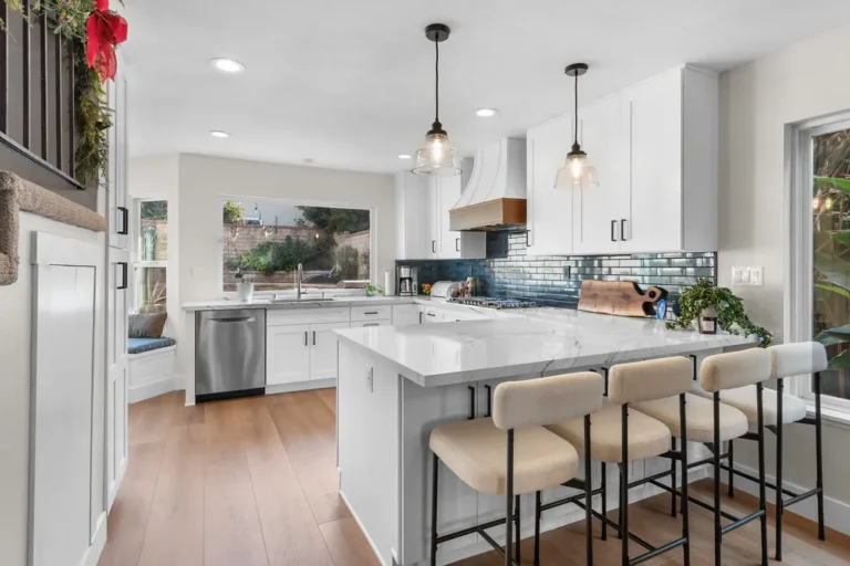 Bright white shaker kitchen with marble peninsula, teal subway tile backsplash, and cream bar stools in Moorpark by RnD Builders Inc