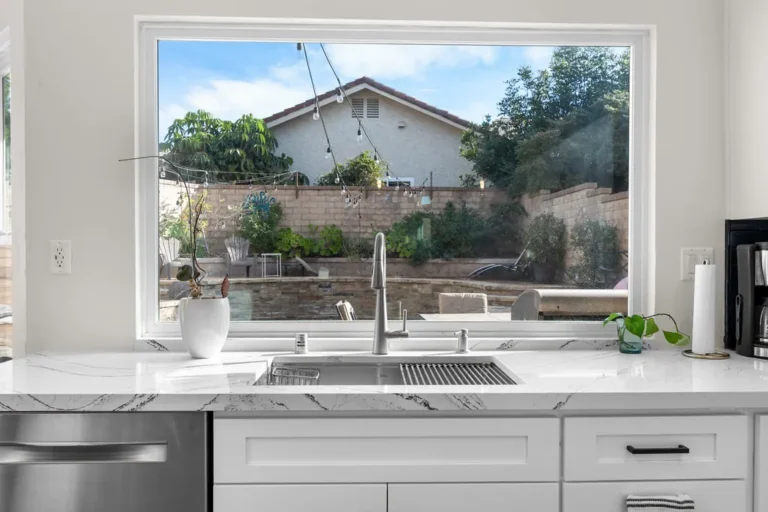 White shaker kitchen with quartz countertop, undermount sink, and large picture window overlooking backyard in Moorpark by RnD Builders Inc
