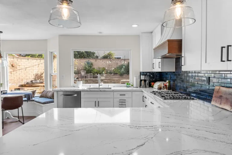 White shaker kitchen with marble quartz island, navy subway tile backsplash, and glass pendants by RnD Builders Inc