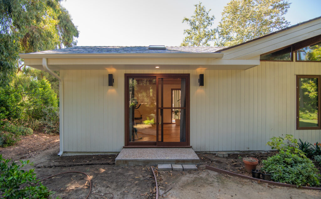 Exterior of Single-story Home Addition in Santa Rosa Valley Exterior of single-story home addition with large wood-framed sliding glass door and vertical board siding in Santa Rosa Valley by RnD Builders Inc