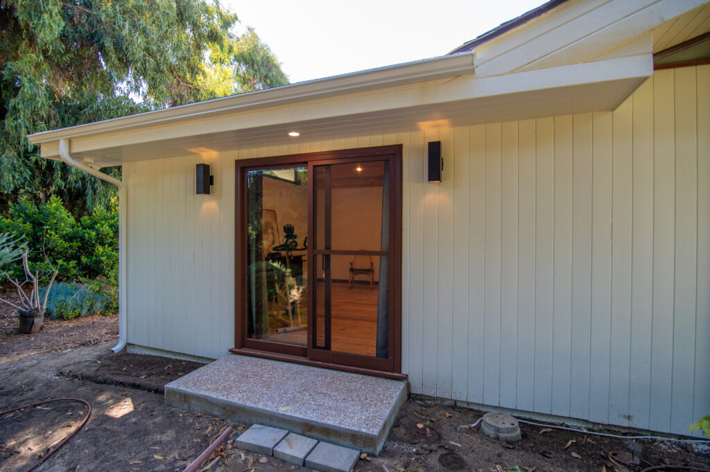 Santa Rosa Valley Home Addition Exterior of white board-and-batten ADU addition with dark wood-framed sliding glass door in Santa Rosa Valley by RnD Builders Inc