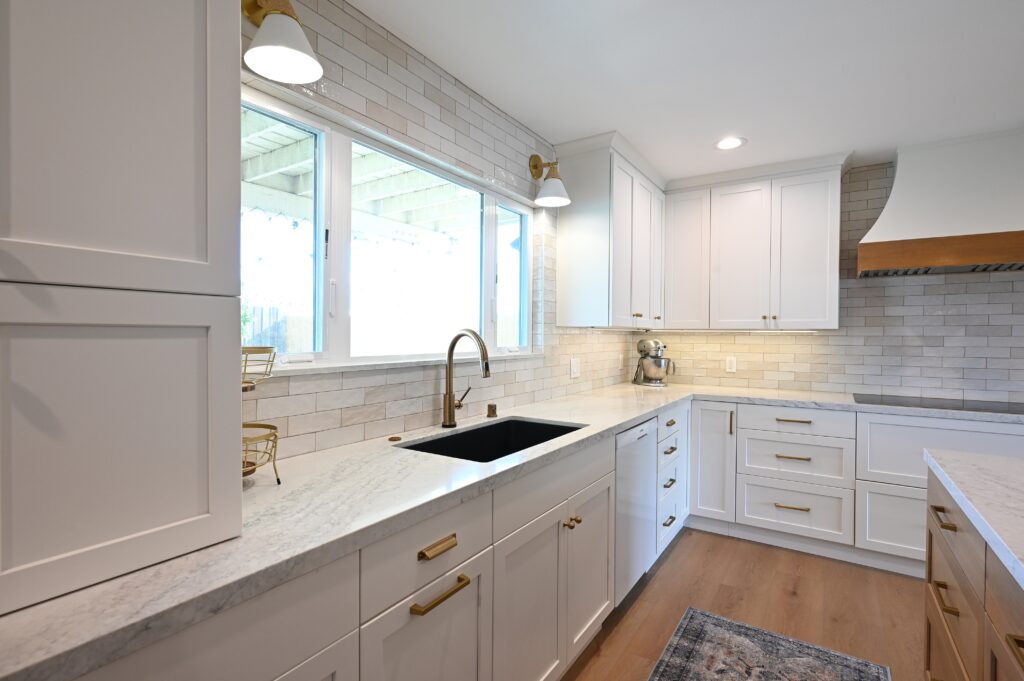White Shaker Kitchen with Marble Countertops in Thousand Oaks White shaker kitchen with marble countertops, black undermount sink, and brass hardware in Thousand Oaks by RnD Builders Inc