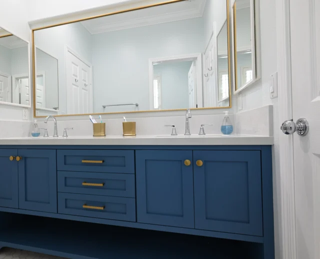 Double-sink Bathroom Vanity with Navy Blue Shaker Cabinets Double-sink bathroom vanity with navy blue shaker cabinets, white quartz countertop, and gold-framed mirrors by RnD Builders Inc