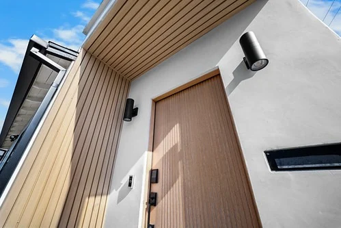 Modern Home Entry with Wood-grain Front Door in Manhattan Beach Modern home entry with wood-grain front door, vertical timber cladding, and black cylinder wall sconces in Manhattan Beach by RnD Builders Inc