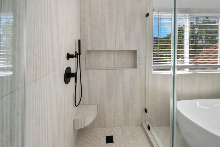 Walk-in shower with cream textured tile, matte black fixtures, built-in niche, and herringbone floor by RnD Builders Inc