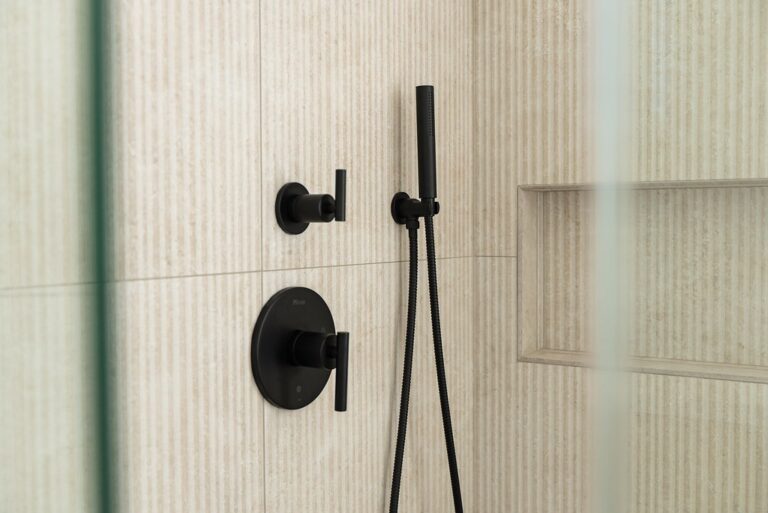Matte black shower fixtures with hand wand on ribbed cream tile wall with built-in niche by RnD Builders Inc