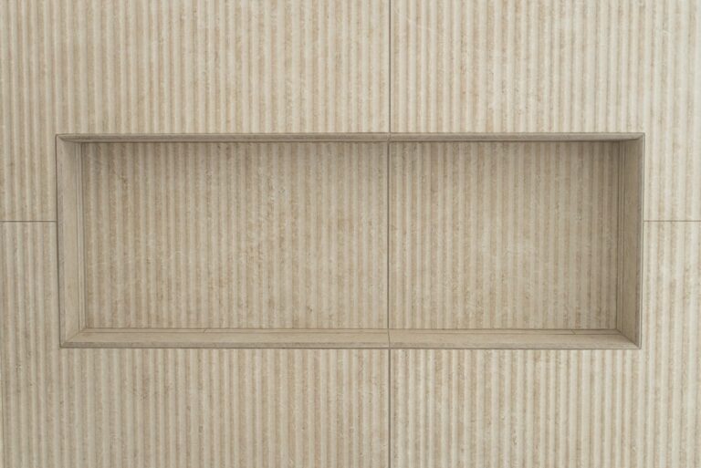 Recessed shower niche in beige fluted stone-look large-format tile wall by RnD Builders Inc