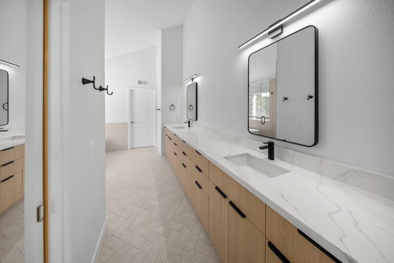 Modern double-vanity bathroom with light wood cabinetry, white quartz countertops, and matte black fixtures by RnD Builders Inc