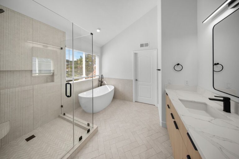 Luxury primary bathroom with freestanding soaking tub, glass shower enclosure, and wood vanity by RnD Builders Inc