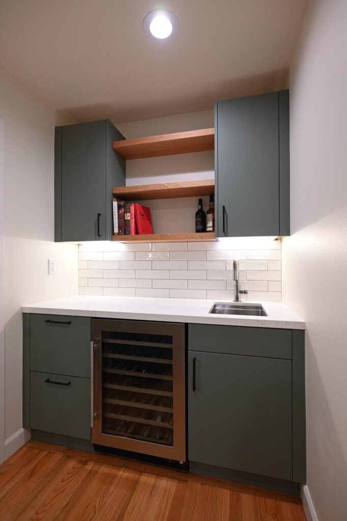 Thousand Oaks green kitchen: Compact wet bar with sage green flat-front cabinets, wine cooler, and white subway tile backsplash in Thousand Oaks by RnD Builders Inc