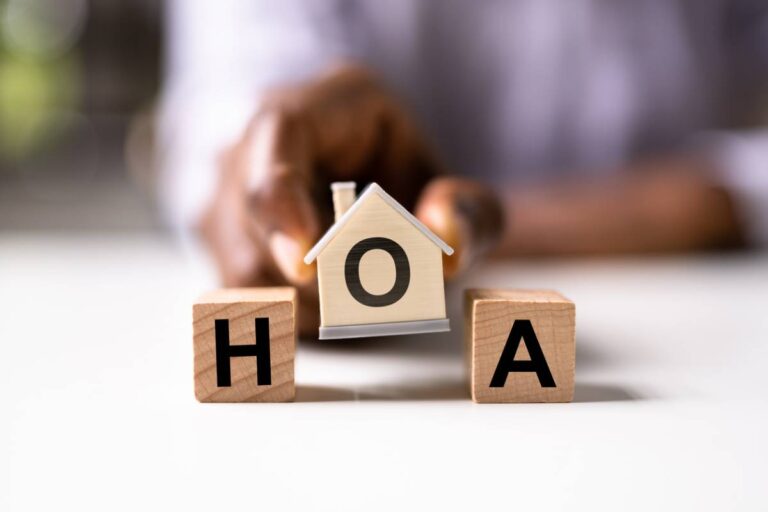 Close-up of wooden house model and letter blocks showing HOA, symbolizing HOA regulations for homeowners.